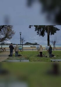 Artists painting by the sea in Garitsa, with Corfu's Old Fortress visible in the background.